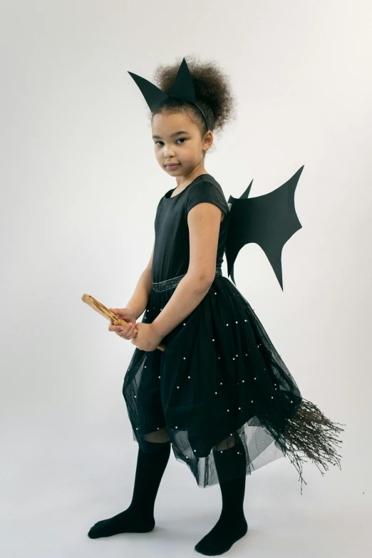 a little girl dressed up as a bat, a picture, pose 4 of 1 6, wearing a dress made of beads, matte black paper, flying on the broom