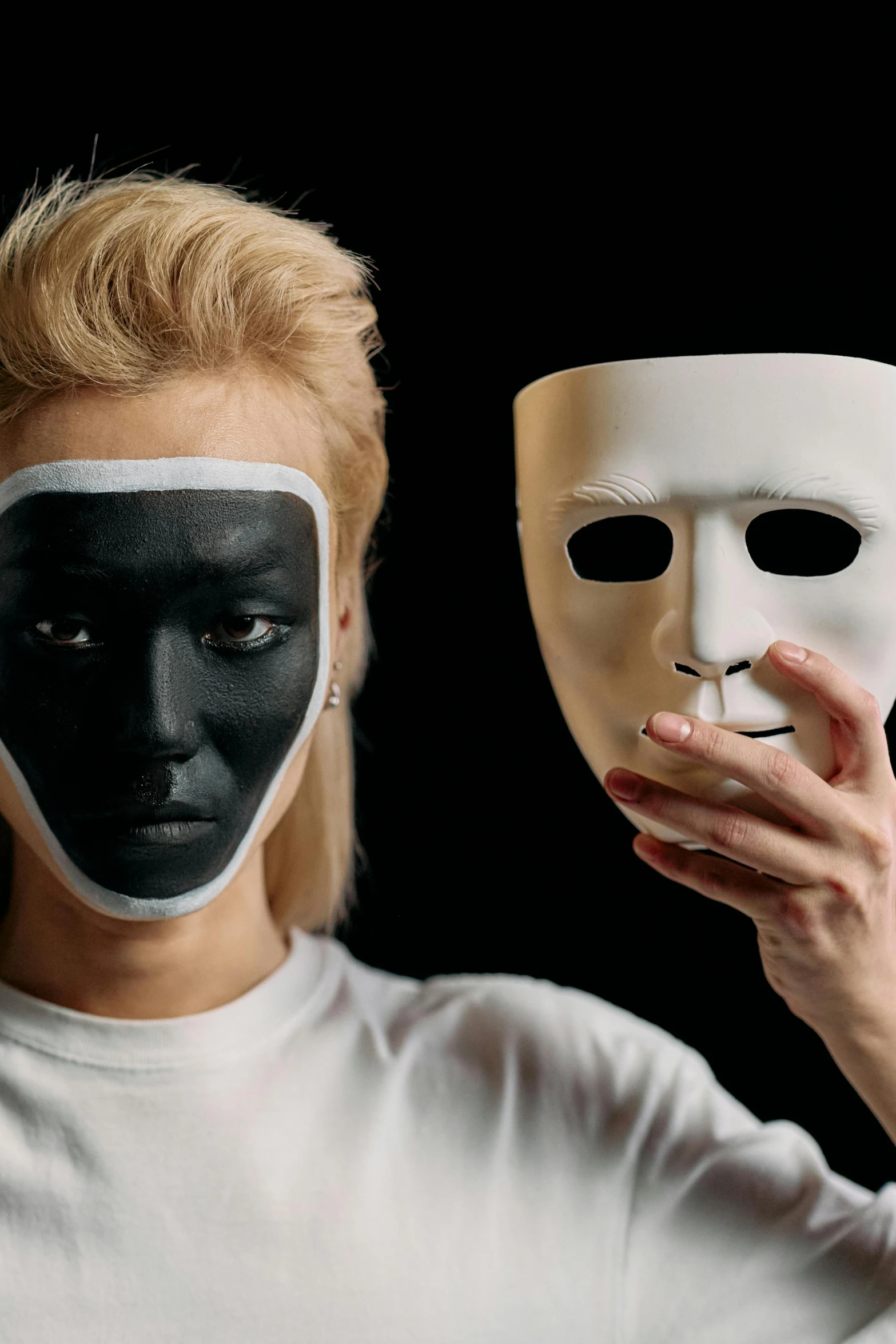 a woman holding a white mask in front of her face, a black and white photo, trending on pexels, antipodeans, half robot and half woman, painted black, with black, college