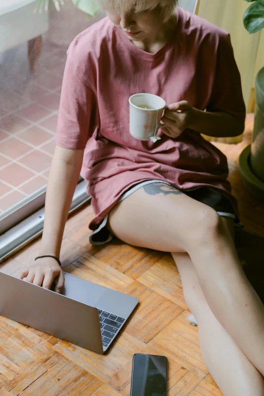 a woman sitting on the floor with a laptop and a cup of coffee, inspired by Elsa Bleda, trending on pexels, renaissance, of taiwanese girl with tattoos, brown and pink color scheme, dressed in a top and shorts, window