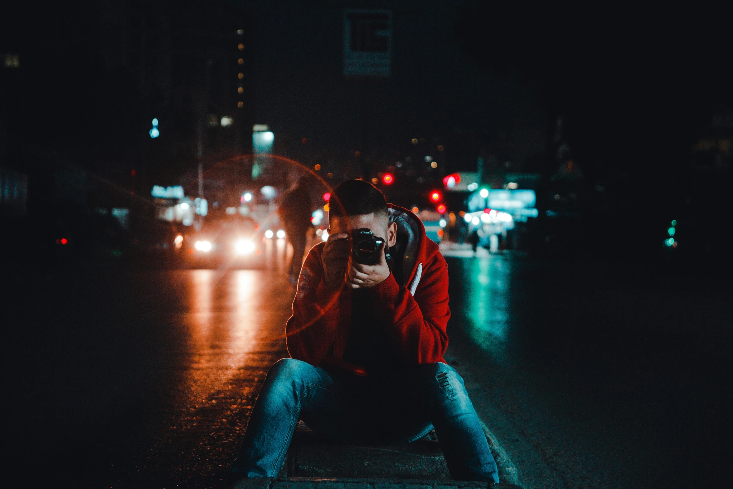 a person sitting on a curb with a camera, a picture, by Alejandro Obregón, unsplash contest winner, red lights, profile picture 1024px, holding it out to the camera, low lights
