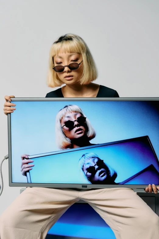 a woman sitting on a chair holding a television, an album cover, inspired by Gao Cen, unsplash, video art, wearing mirrored sunglasses, two models in the frame, close up to the screen, ultrawide image