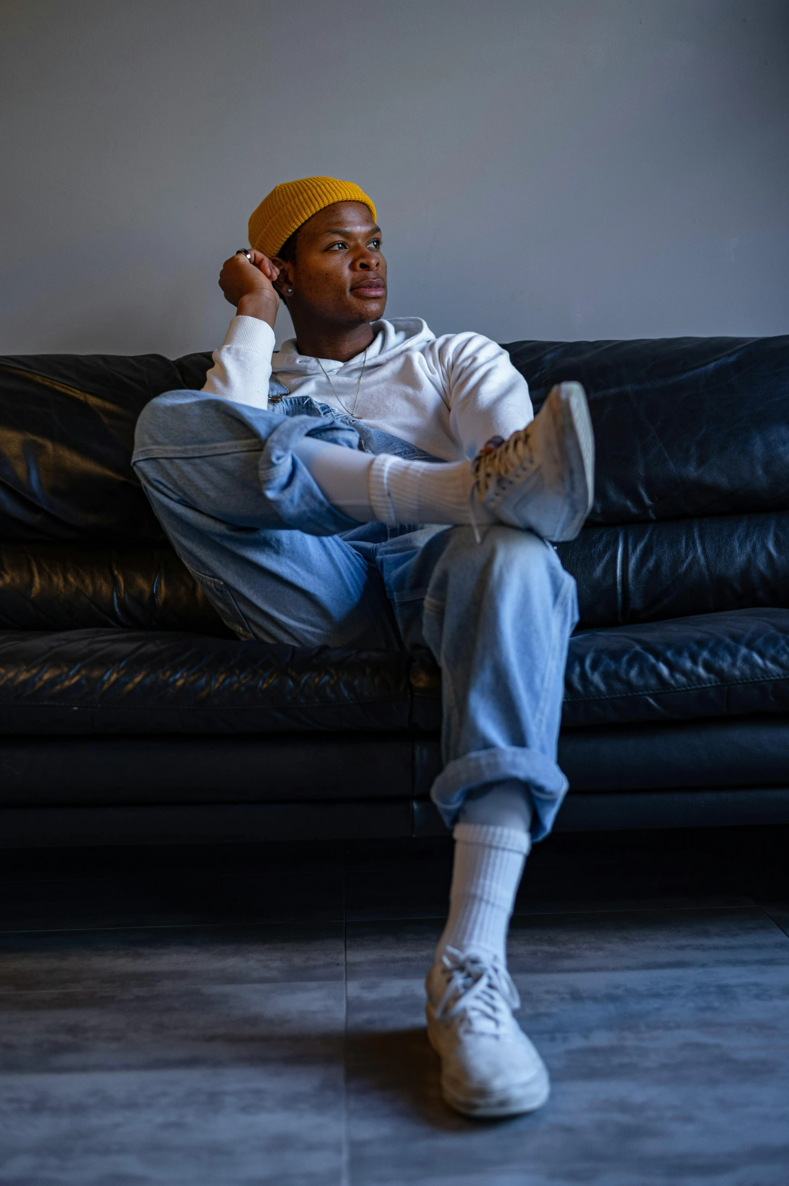 a man sitting on a couch talking on a cell phone, an album cover, by Cosmo Alexander, trending on pexels, baggy jeans, confident pose, with hat, non binary model