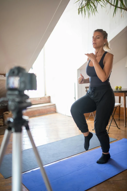 a woman standing on a yoga mat in front of a camera, teaching, thumbnail, multiple stories, knee