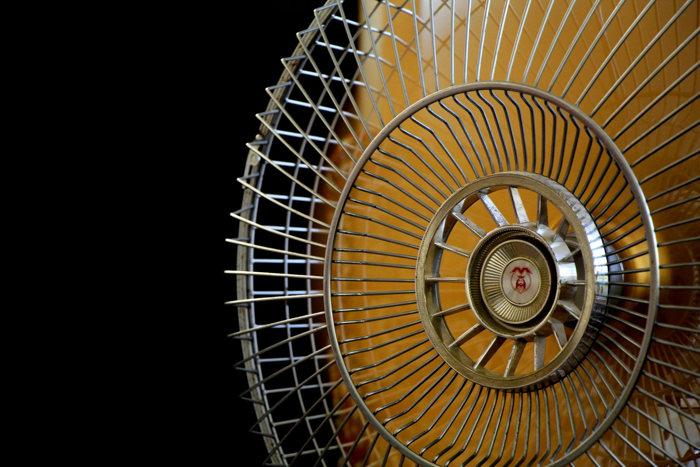 a metal fan sitting on top of a wooden floor, by Jan Rustem, pexels contest winner, kinetic art, air conditioner, gold, circular, with a black background