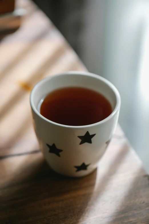 a cup of tea sitting on top of a wooden table, by Jessie Algie, trending on pexels, tiny stars, rum, profile image, soup