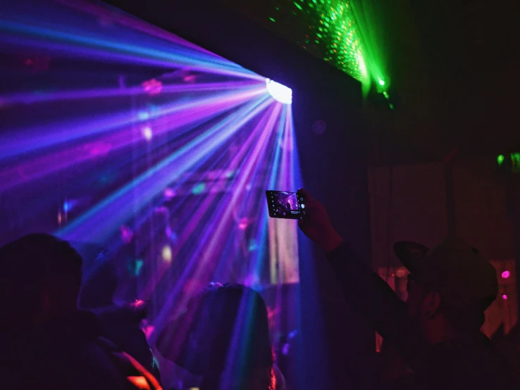 a person taking a picture of a light show, by Joe Bowler, pexels, holography, dive bar with a karaoke machine, “house music rave with dancers, deep colour, closed limbo room