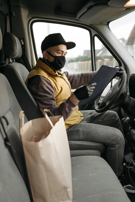 a man sitting in the driver's seat of a truck, pexels contest winner, renaissance, white man with black fabric mask, delivering mail, yellow and charcoal leather, wearing a vest