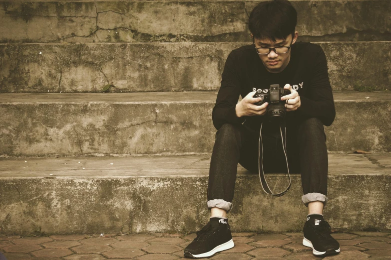 a man sitting on some steps holding a camera, pexels contest winner, realism, video game consoles, keng lye, teenage boy, looking down on the camera