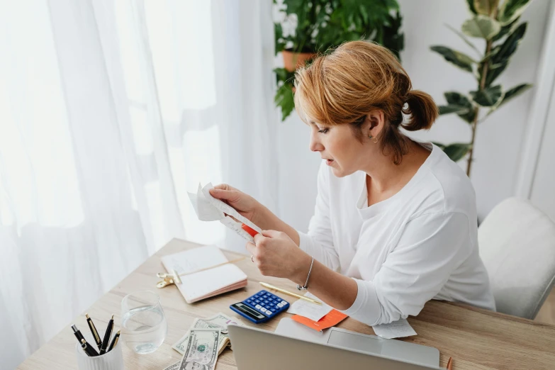 a woman sitting at a table with a laptop and a calculator, pexels contest winner, cash on a sidetable, avatar image, nursing, high quality image