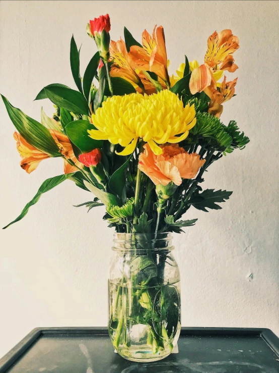 a vase filled with flowers sitting on top of a table, yellow orange, inside a glass jar, designed for cozy aesthetics!, vibrantly lush