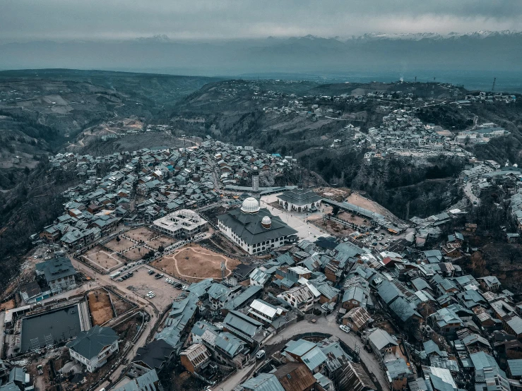 an aerial view of a town surrounded by mountains, by Muggur, pexels contest winner, hurufiyya, located in hajibektash complex, grey, background image, ayanamikodon and irakli nadar