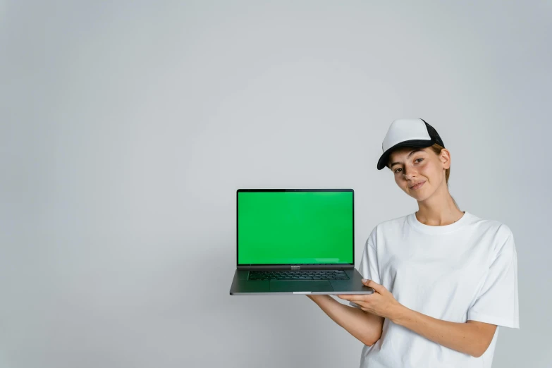 a woman holding a laptop with a green screen, pexels, wearing baseball cap, on a gray background, background image, holding a stuff