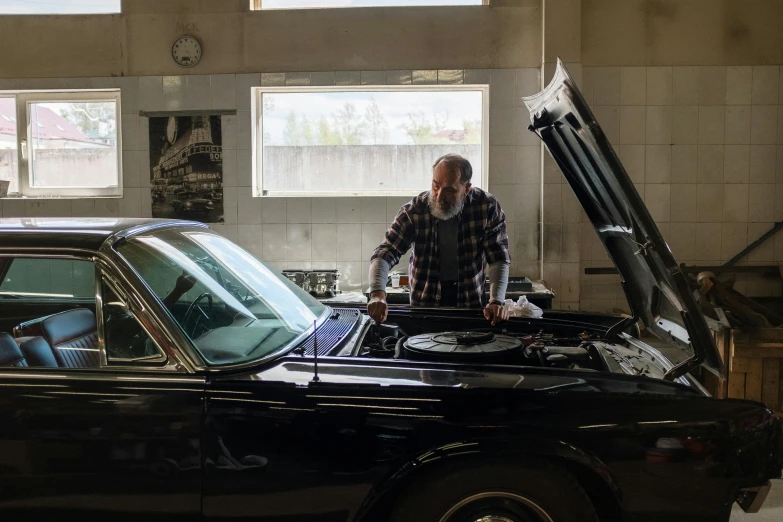 a man standing next to a black car in a garage, balding older cyborg repairing, promo image, top down, profile image