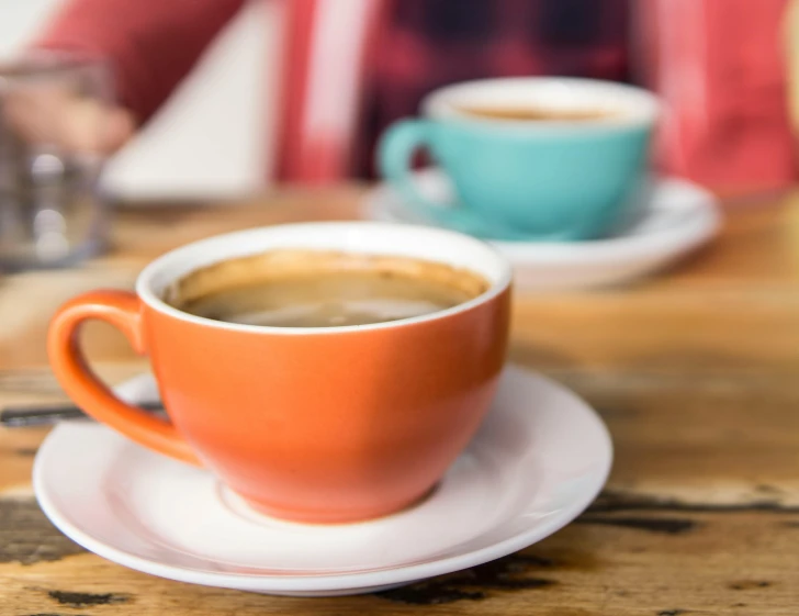 a person sitting at a table with a cup of coffee, teal and orange, two cups of coffee, zoomed in, colourful