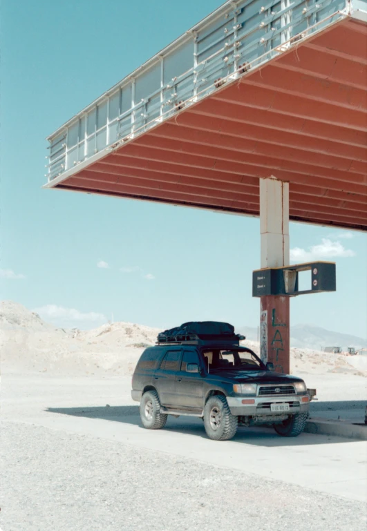 a car is parked in front of a gas station, by Nathalie Rattner, conceptual art, gulf war photography, overpass, mexican desert, rinko kawauchi