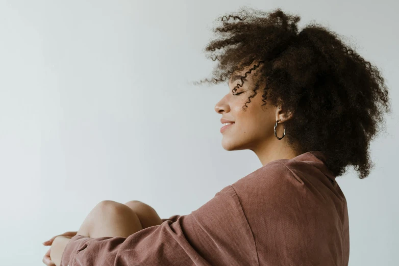 a woman with curly hair sitting on the floor, trending on pexels, left profile, pictured from the shoulders up, happy cozy feelings, ad image