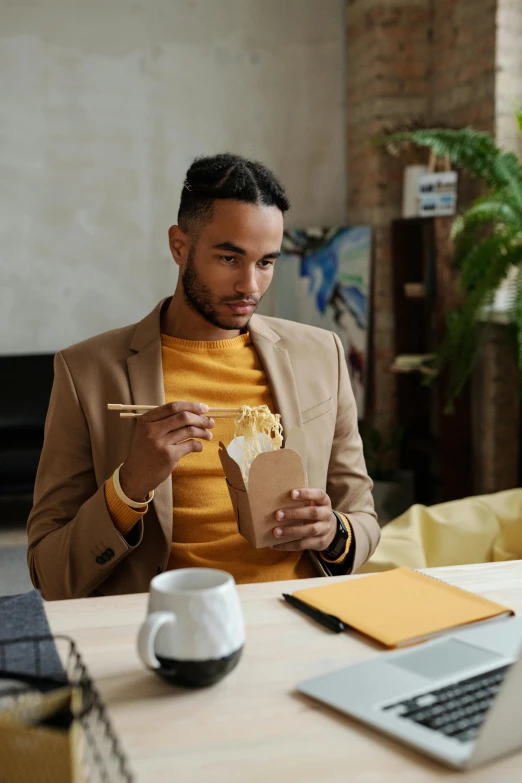 a man sitting at a table in front of a laptop, eating noodles, tailored clothing, tan suit, millennial vibes