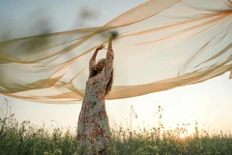 a woman holding a sheer over her head in a field, by Jessie Algie, pexels contest winner, arabesque, swirling fabric, medium format. soft light, evening sunlight, ilustration