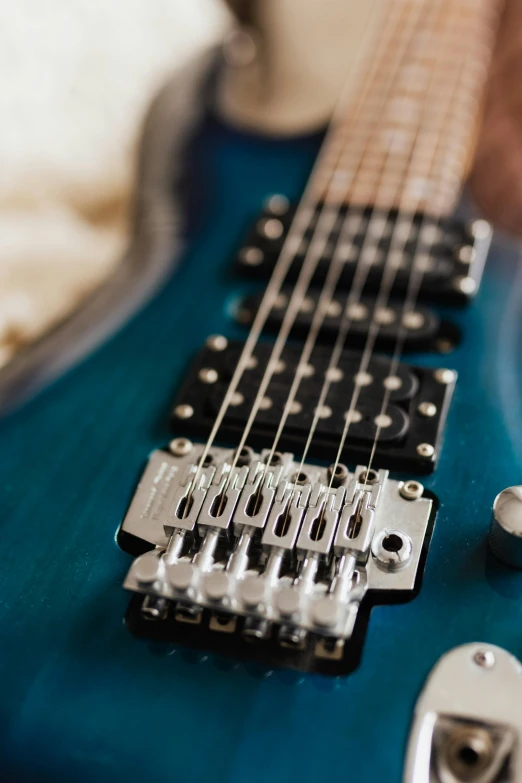 a blue electric guitar sitting on top of a bed, zoomed in, teal, detailed product shot, guitar shape build