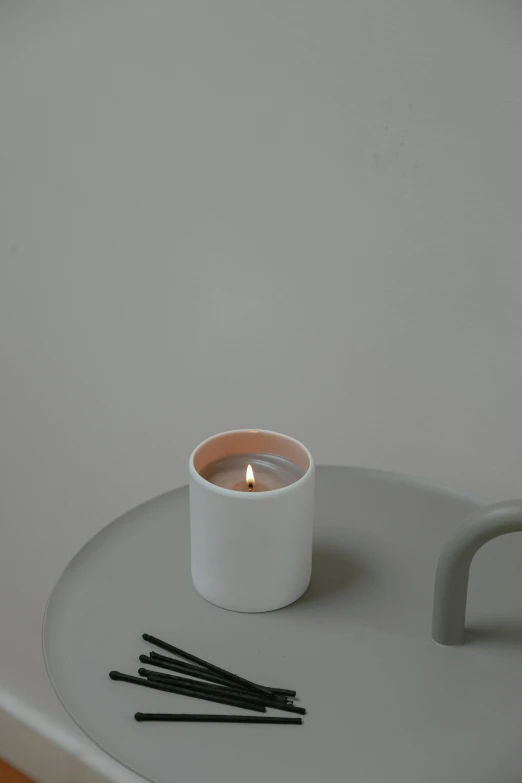 a candle sitting on top of a white table, inspired by Hendrik Gerritsz Pot, on a gray background, with a white mug, dwell, middle close up