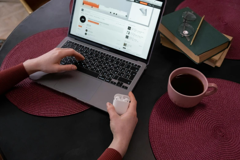 a person sitting at a table using a laptop computer, airpods, white and orange, instagram photo, holding flask in hand