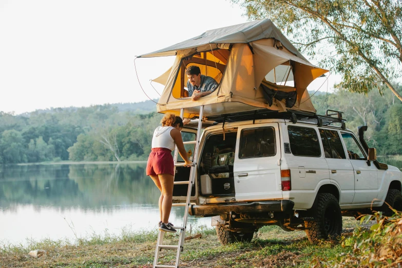 a man standing on top of a ladder next to a white van, by Pamela Ascherson, trending on pexels, interior of a tent, jeep, australian, woman