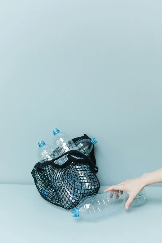 a woman sitting on the floor next to a bag of water, pexels contest winner, plasticien, blue silver and black, netting, hand on table, plain background