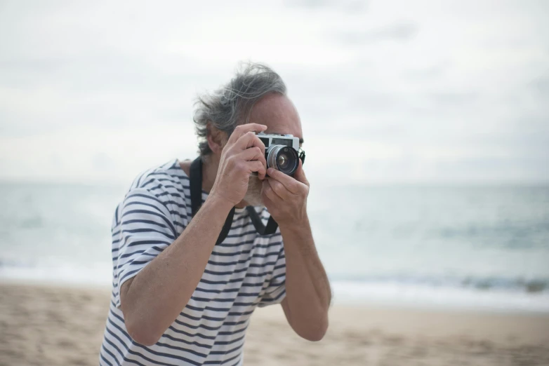 a man taking a picture with a camera on the beach, inspired by Max Dupain, unsplash, photorealism, grey beard, medium format, colour photograph