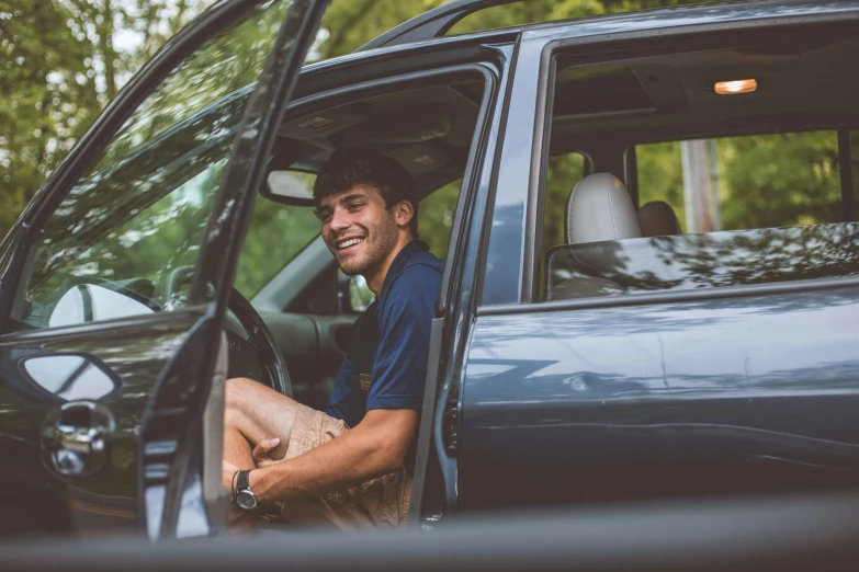 a man sitting in the driver's seat of a car, by Matt Cavotta, smiling down from above, college, avatar image