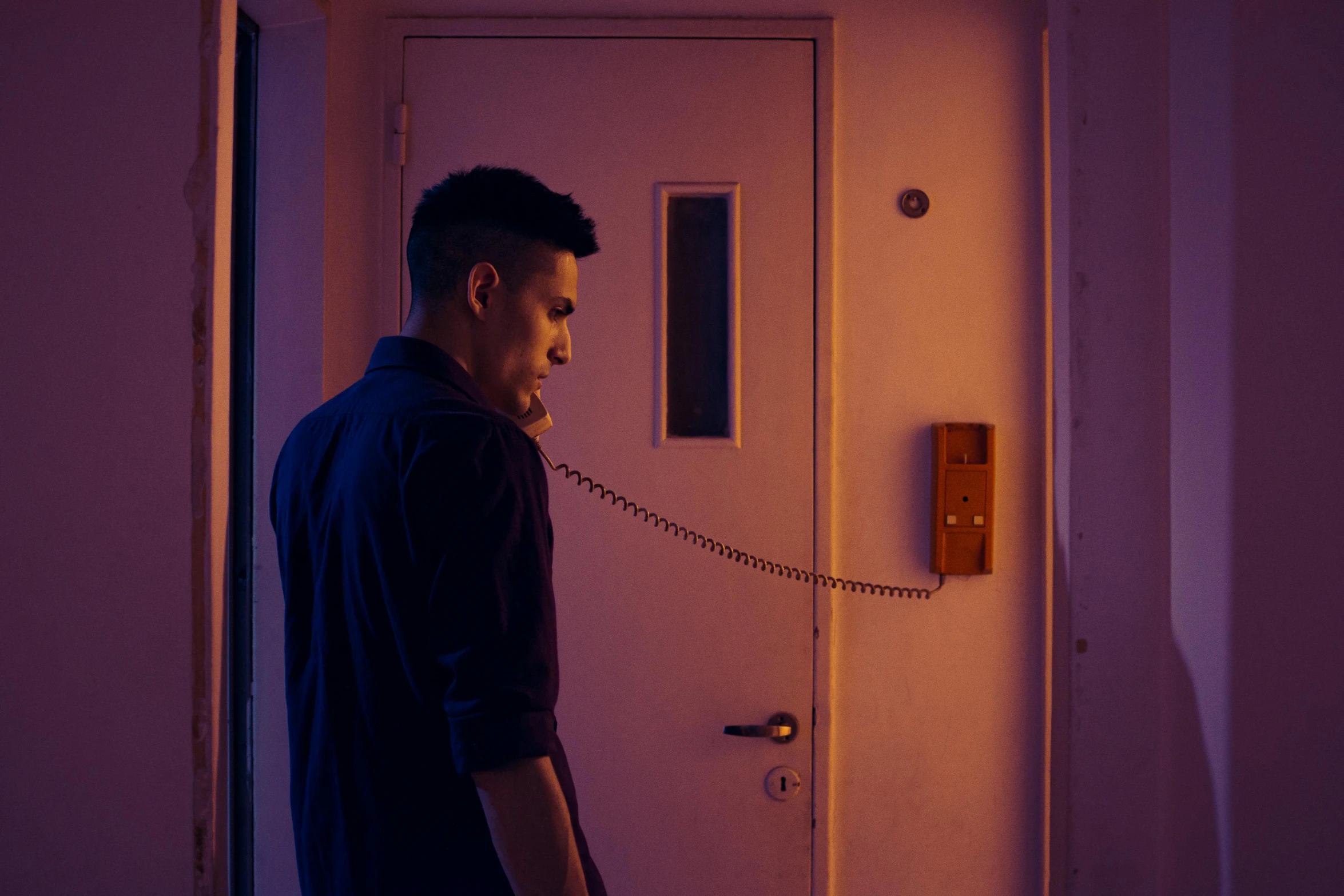 a man standing in front of a door talking on a phone, inspired by Nan Goldin, pexels contest winner, serial art, purple ambient light, lee madgwick & liam wong, **cinematic, wong kar wai