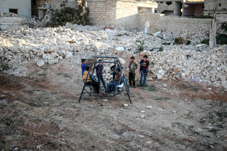 a group of men standing next to a pile of rubble, an album cover, dau-al-set, swings, photographed for reuters, kids playing, photo taken in 2 0 2 0