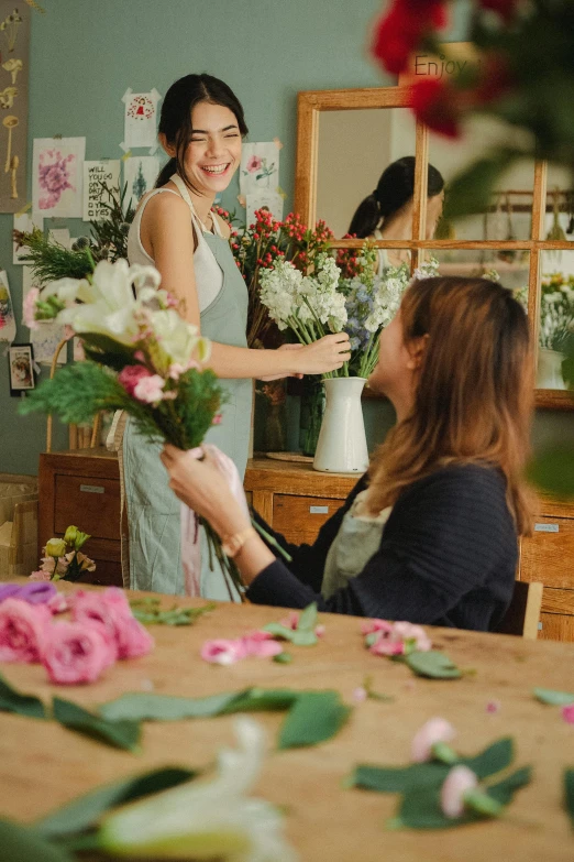 a woman standing in front of a table with flowers, smiling at each other, flower shop scene, inspiration, production photo