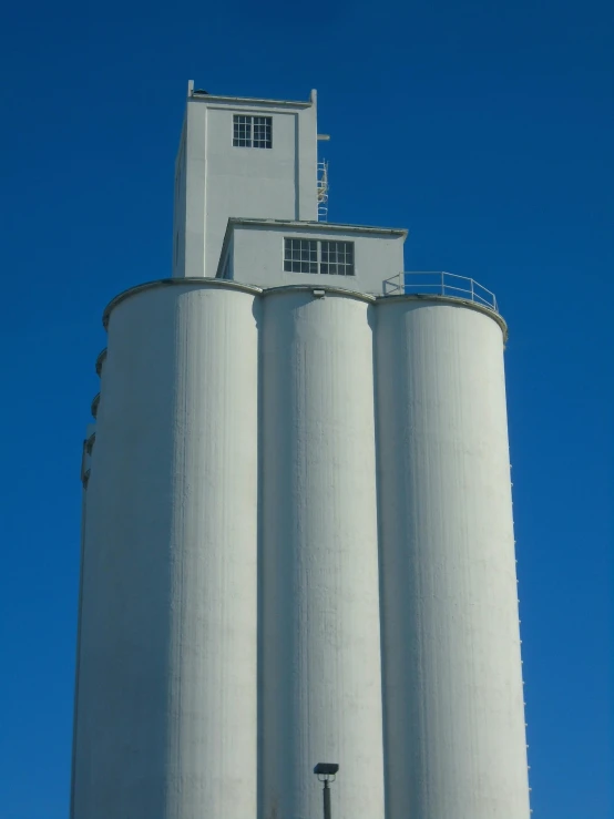 a large white grain silo in front of a blue sky, unsplash, modernism, multiple stories, tyndall rays, high resolution image