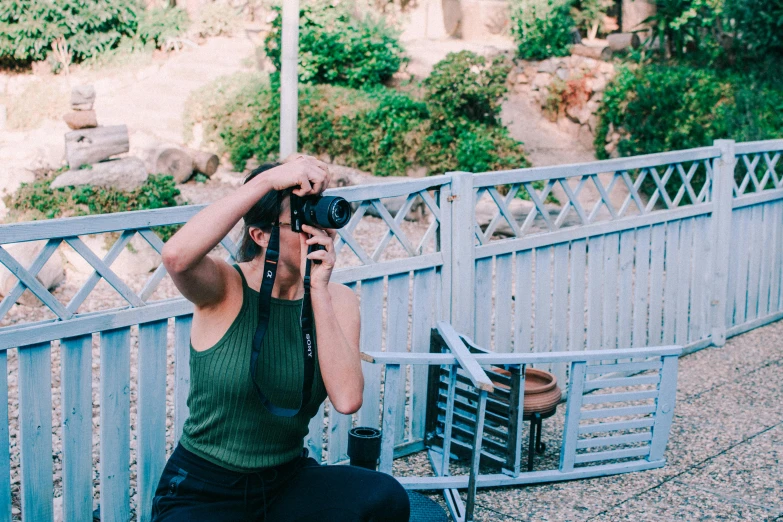 a woman sitting on a bench holding a camera, a picture, by Julia Pishtar, unsplash, botanic garden, sydney hanson, making of, looking down on the camera