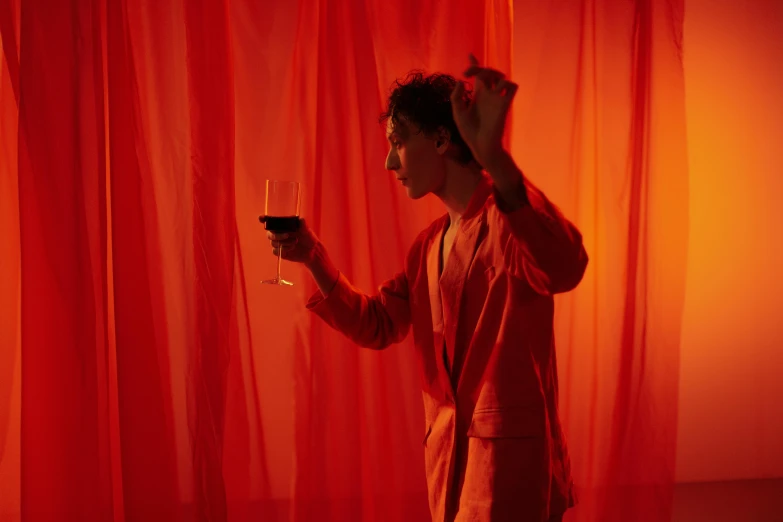 a man standing in front of a red curtain holding a glass of wine, inspired by Georges de La Tour, pexels contest winner, cai xukun, ryan mcginley, still from a music video, complementary colour