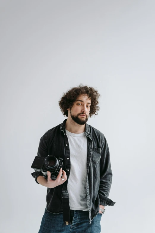 a man standing with a camera in his hand, messy curly hair, white backdrop, captured on canon eos r 6, gif