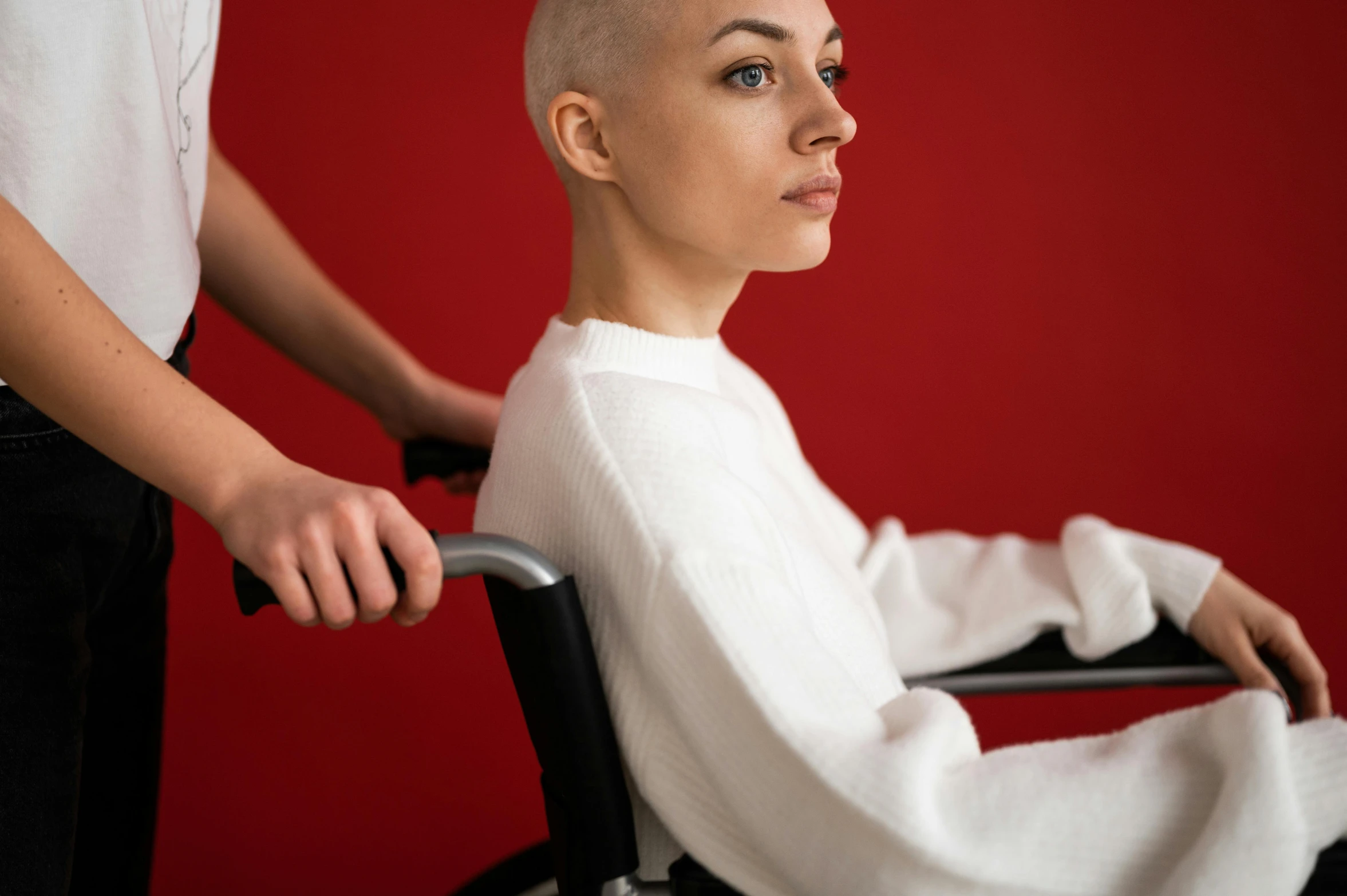 a woman sitting in a wheel chair next to a man, by Julia Pishtar, trending on pexels, hurufiyya, no hair completely bald, striking colour, medical image, white hime cut hairstyle