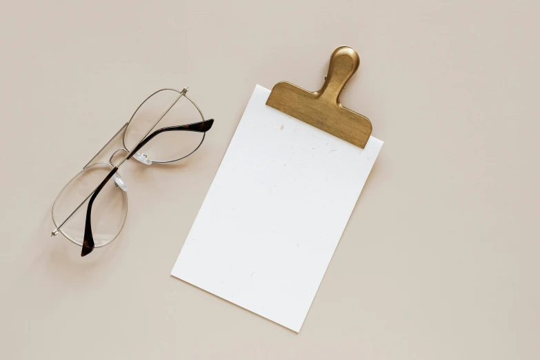 a clipboard sitting on top of a table next to a pair of glasses, trending on pexels, beige and gold tones, card template, white backround, background image