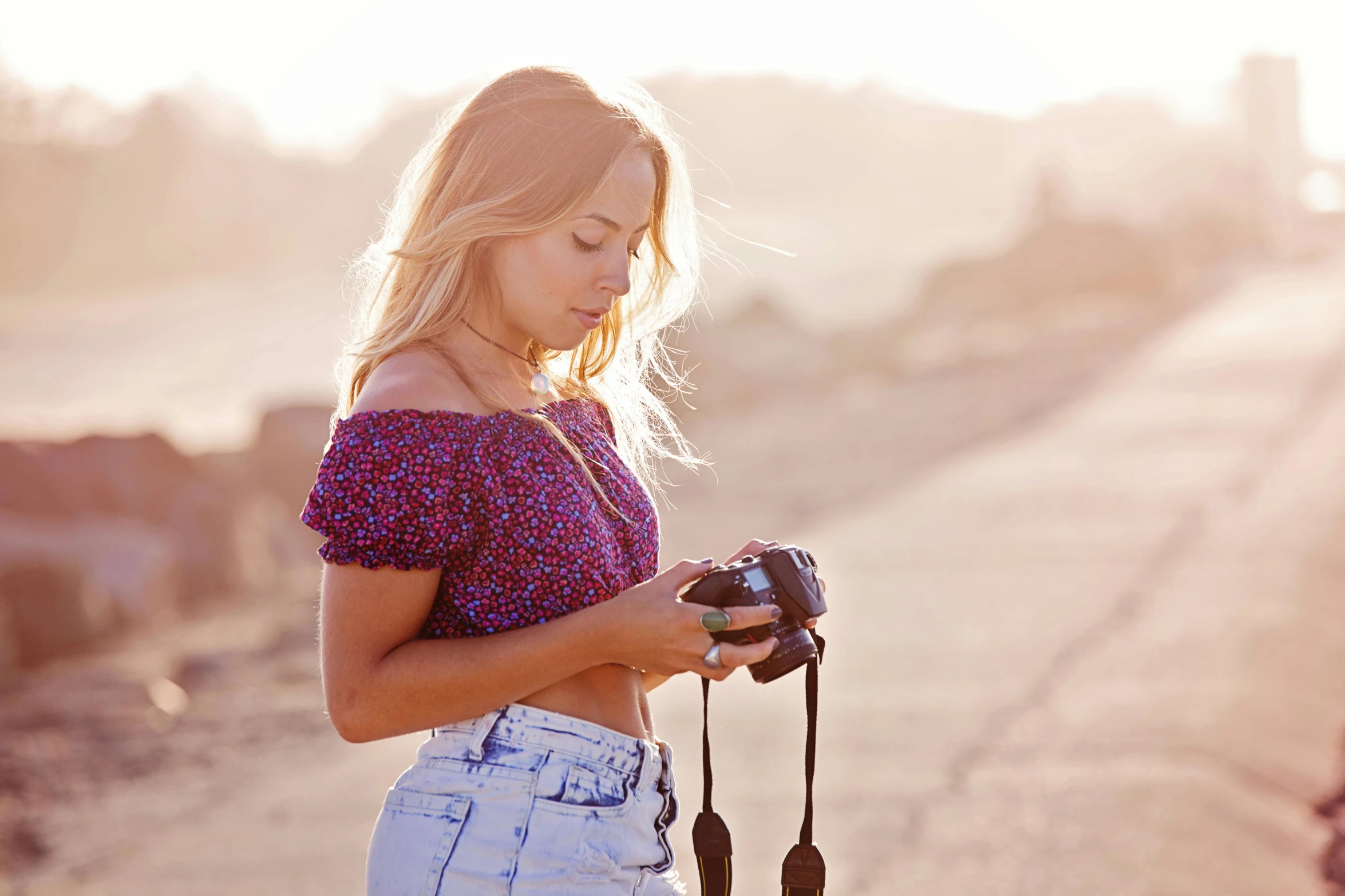 a woman standing on a dirt road holding a camera, by Julia Pishtar, crop top, sunny lighting, print, profile image