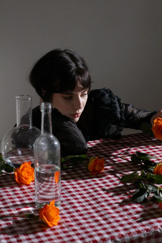 a woman sitting at a table with a red and white checkered table cloth, an album cover, by Winona Nelson, pexels contest winner, timothee chalamet, vases and bottles, laying on roses, looking away