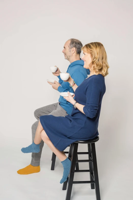 a man and a woman sitting on a stool, with a white mug, lynn skordal, brett goldstein, profile image