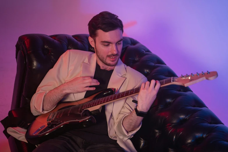 a man sitting in a chair playing a guitar, charli bowater, on a couch, profile pic, bassist