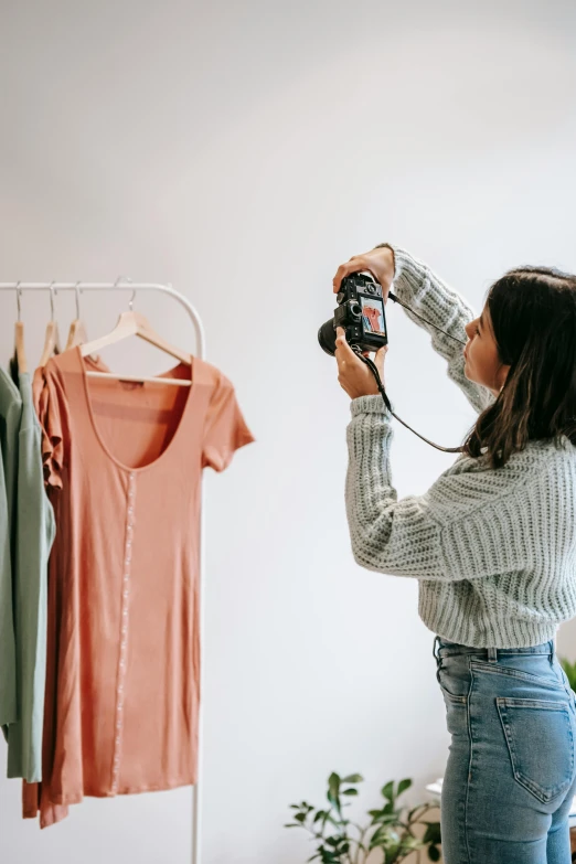 a woman standing in front of a clothing rack holding a camera, girl creates something great, full product shot, wearing a cute top, low colour