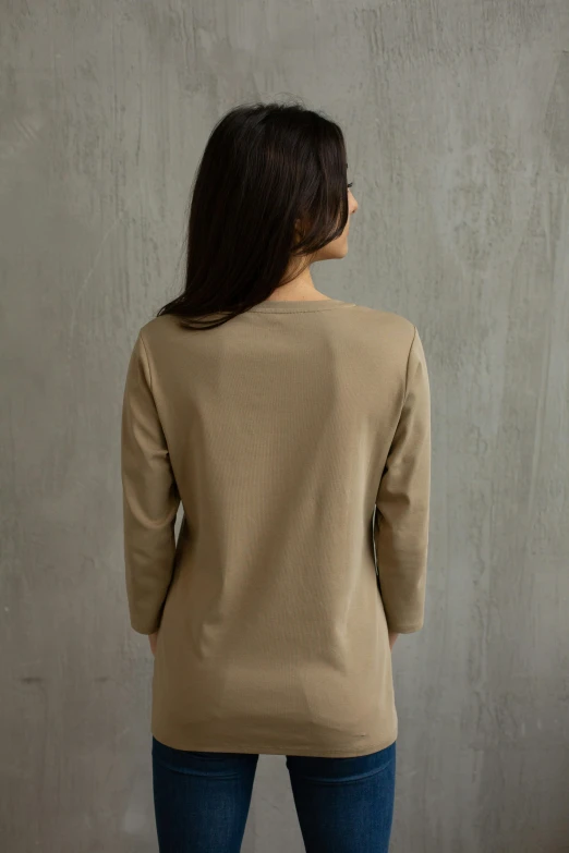 a woman standing in front of a concrete wall, brown shirt, back facing, product shot, taupe