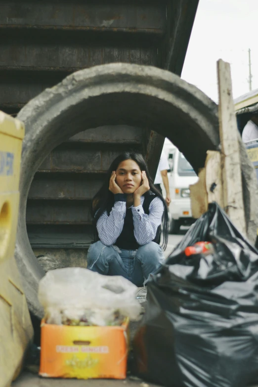 a woman sitting on the ground next to a pile of garbage, cindy avelino, kodak portra, concerned expression, in a city