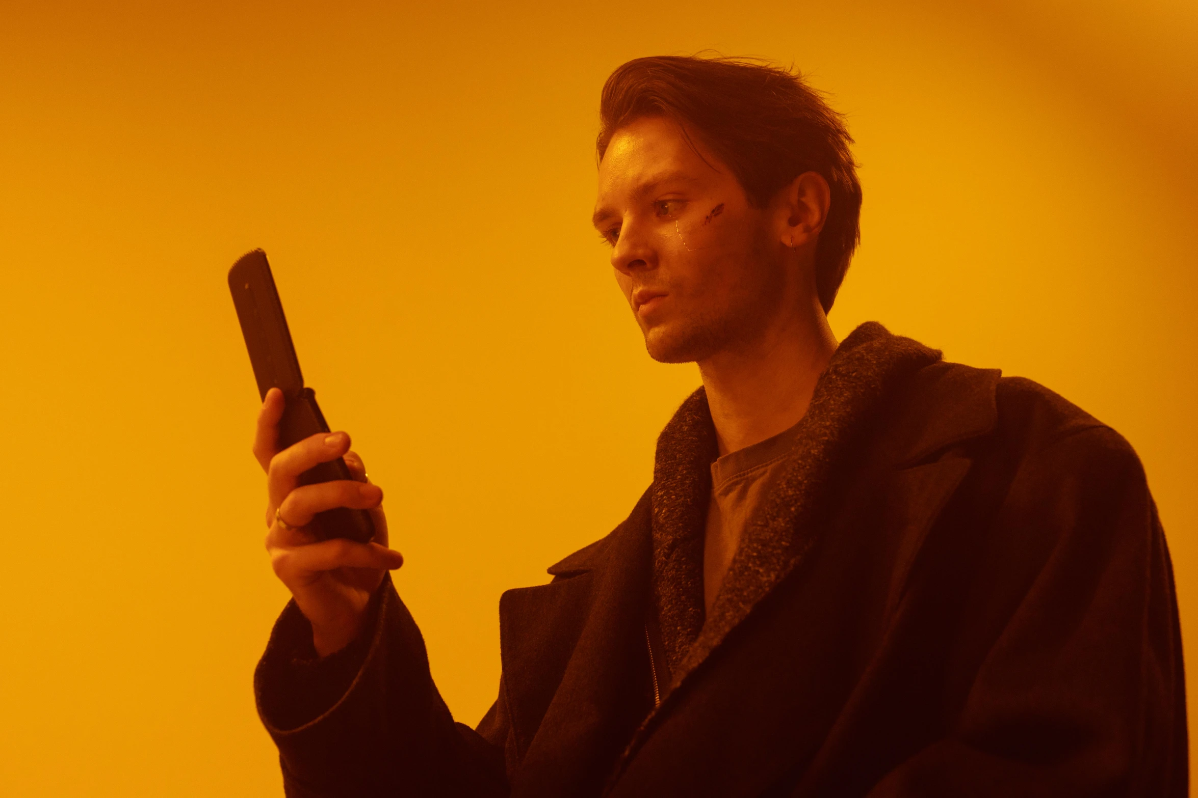 a man in a robe holding a cell phone, unsplash, bauhaus, yellow lighting from right, julian ope, he is wearing a brown sweater, cyber western