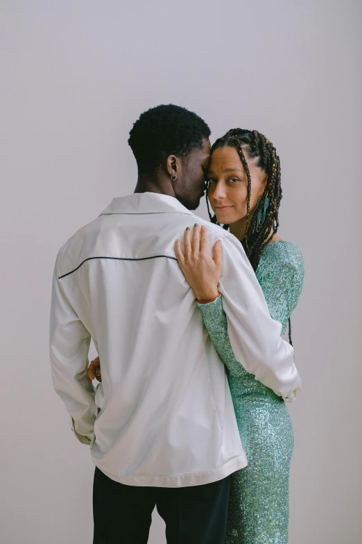a man standing next to a woman in a green dress, holding each other, off - white collection, loving embrace, afar