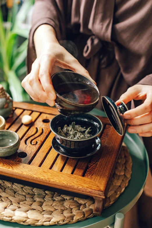 a person pouring tea into a bowl on top of a table, inspired by Cui Bai, wearing a black robe, herbs, promo image, thumbnail