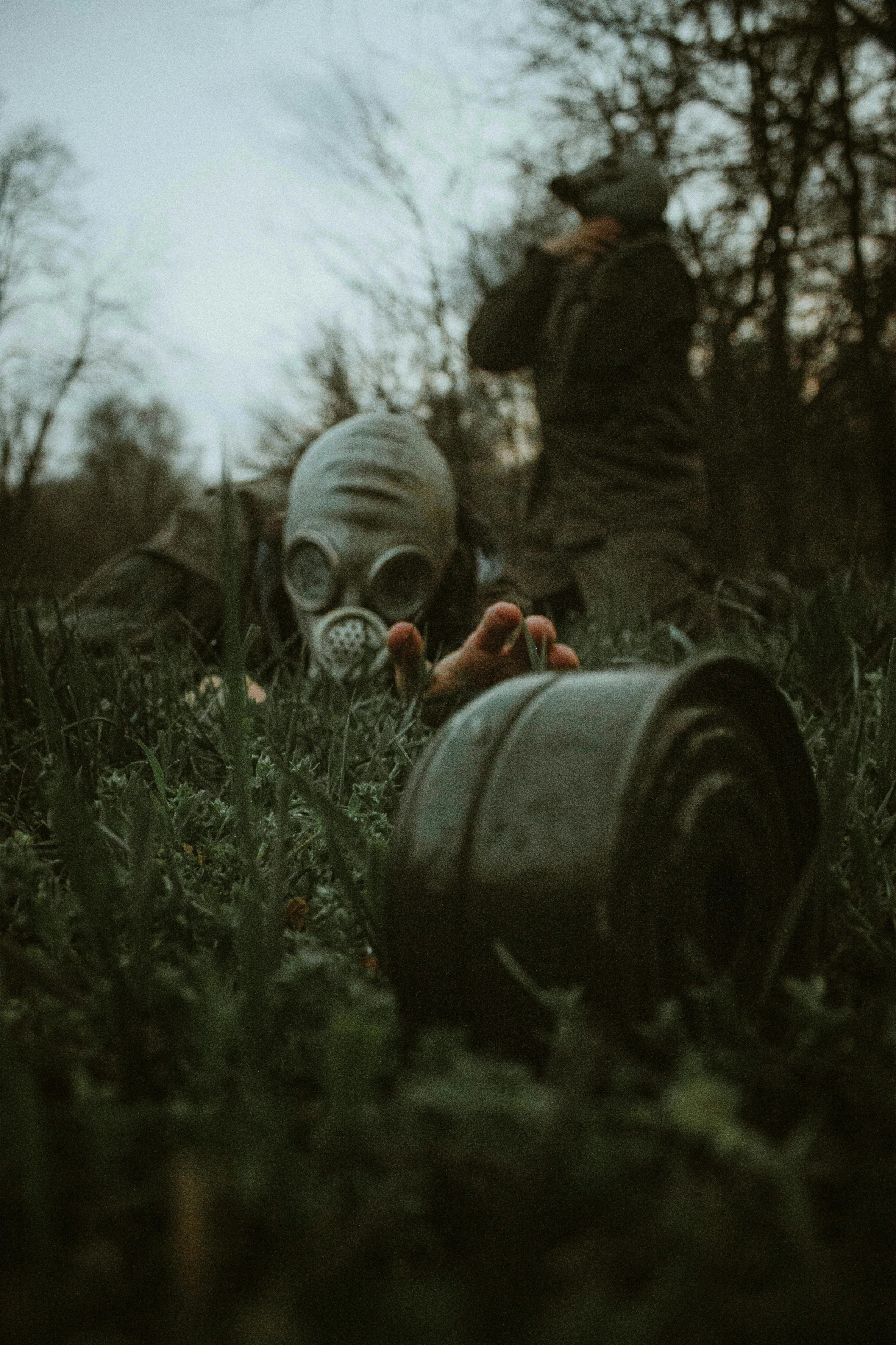 a person in a gas mask laying in the grass, by Adam Marczyński, pexels contest winner, desolate with zombies, medium shot of two characters, holding a bomb, low quality photo