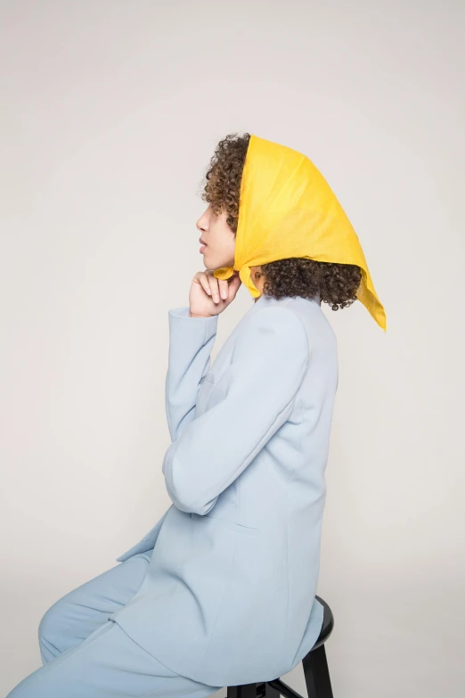 a woman sitting on a stool wearing a yellow hat, an album cover, inspired by Jean-Étienne Liotard, unsplash, head scarf, issey miyake, ( side ) profile, square